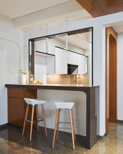 Kitchen breakfast counter with two white stools, pendant lights and a large mirror above cabinetry