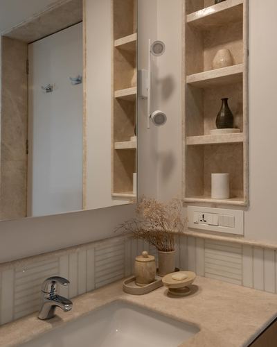 Beige stone bathroom vanity with recessed shelving, mirror, and chrome faucet