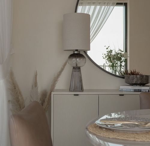 Beige dining sideboard with glass lamp, round mirror, and pampas grass in soft light