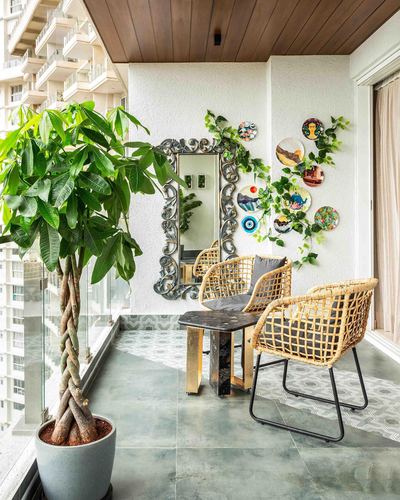 Balcony seating with cane chairs, marble-top brass table, ornate mirror, wall plates and a large potted plant
