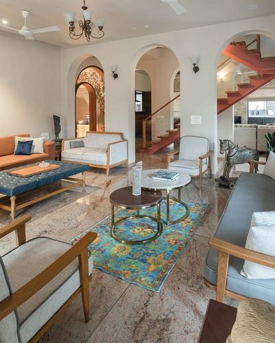 Living room with arched doorways, marble floor, patterned rug, and mixed seating around nested coffee tables