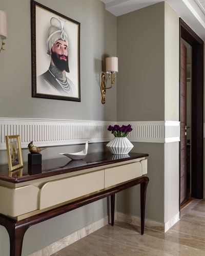 Foyer console table with vase and bird figurine below a turbaned portrait painting and brass sconce