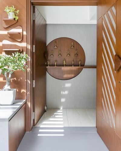 Wooden entryway door opens to a circular niche with brass idols on a fluted grey wall
