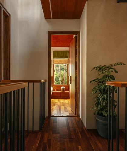 Wooden landing passage with metal railing, potted plant, and open door revealing sunlit bedroom beyond