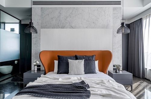 Bedroom with tan leather wingback bed against marble and fluted white wall panels, flanked by pendant lights