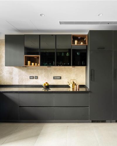 Dark glossy kitchen cabinetry with wood display niches and stone backsplash, brass kettle on counter