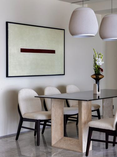 Minimalist dining area with stone-based table, cream chairs, and framed art with maroon stripe