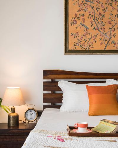 Bedside vignette with lit lamp, alarm clock, slatted wood headboard and breakfast tray on bed