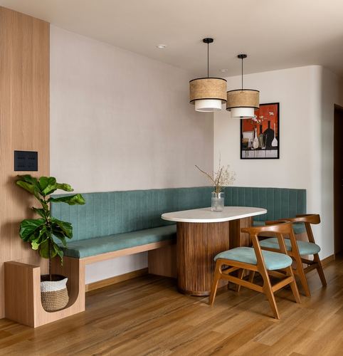 Corner dining nook with teal banquette, fluted wood table, and cane pendant lights