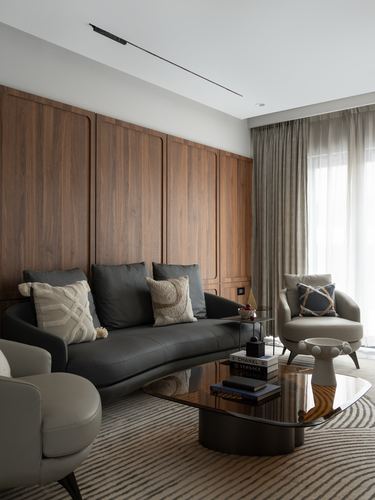 Living room with curved charcoal sofa against walnut panelling and glass coffee table