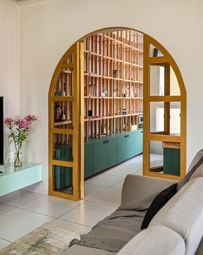 Living room with arched mustard door opening to a slatted wood shelving wall and green cabinets