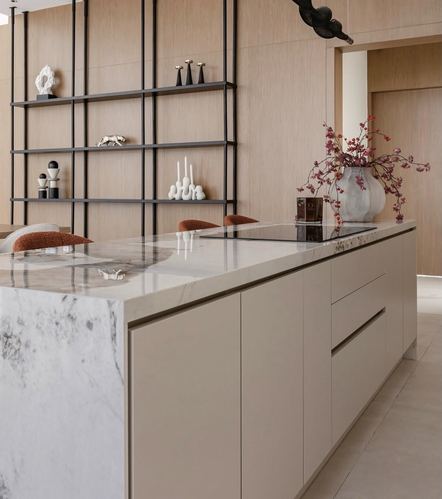 Marble waterfall island in beige kitchen with black shelving and pink floral vase