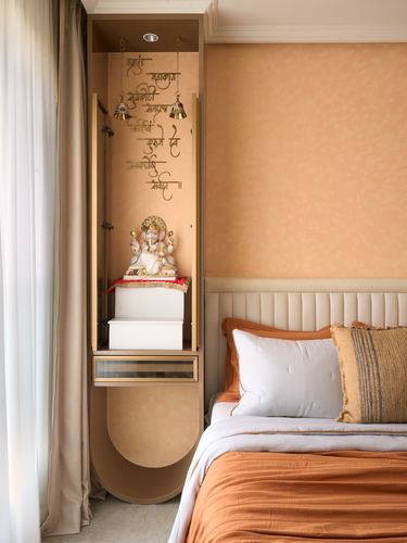 Bedroom pooja niche with Ganesh idol and bells beside a channel-tufted headboard on terracotta wall