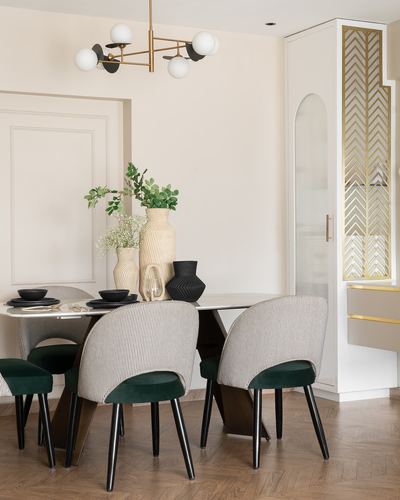 Dining nook with marble table, striped velvet chairs, brass chandelier, and chevron-patterned cabinet door