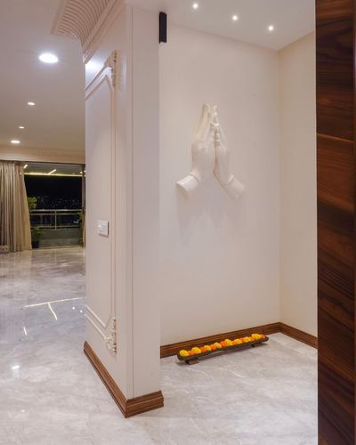 Foyer corner with praying hands wall sculpture above marigold flower tray on marble floor at night