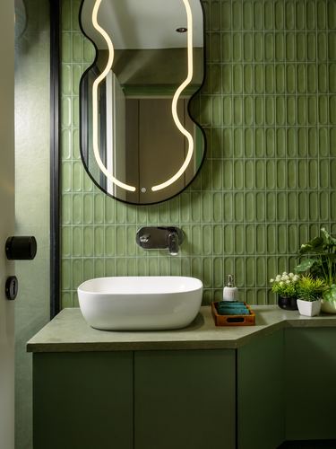 Green ribbed tile bathroom with oval white sink and sculptural backlit mirror