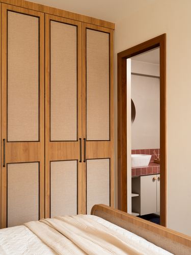 Wooden wardrobe with fabric panels beside doorway view into terracotta-tiled bathroom