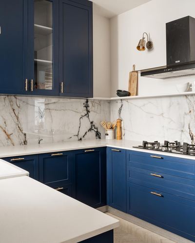 Navy blue L-shaped kitchen with white marble backsplash, brass handles, and black chimney hood