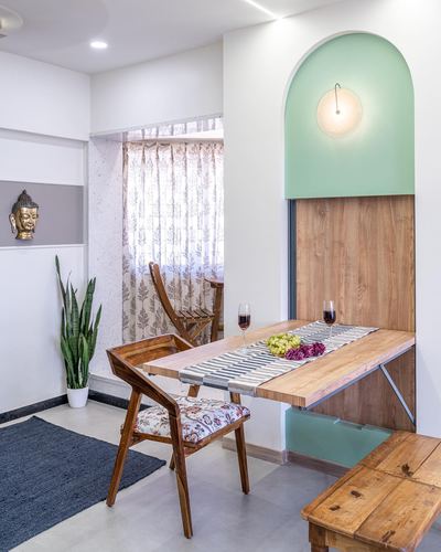 Fold-down wooden dining table set in an arched sage-green niche with wine glasses and fruit