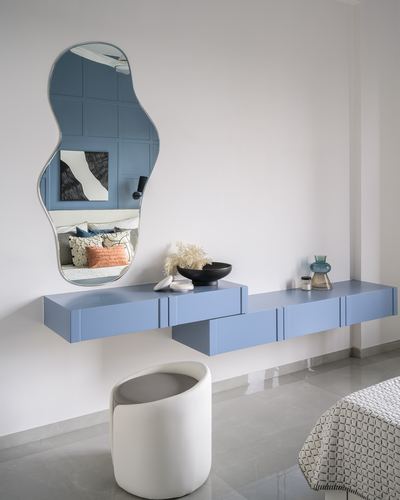 Blue freeform mirror above a floating blue console with a white rounded stool in a bedroom