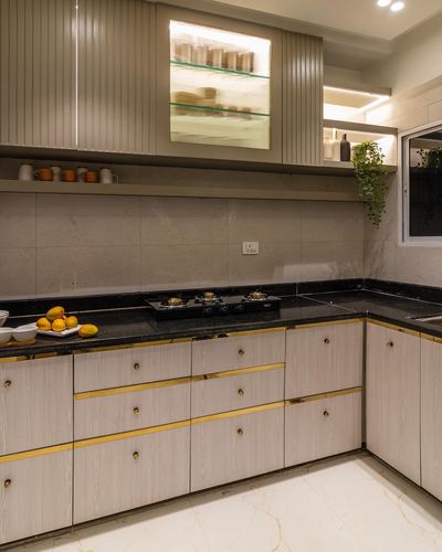 L-shaped kitchen with black countertop, gold-trimmed cabinetry, and glowing display niche