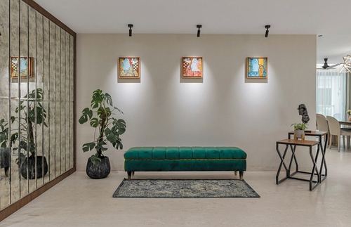 Foyer with teal tufted bench, three lit artworks, mirrored panel wall, and stone floor