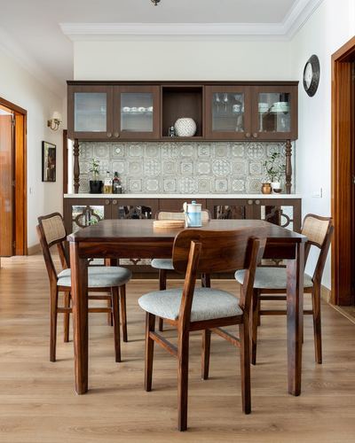 Dining room with wooden table, cane chairs, and tiled backsplash behind cabinetry