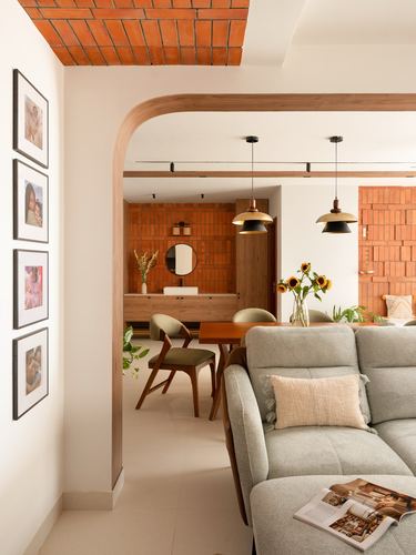 Grey sofa in foreground with arched wooden doorway opening to dining area and exposed brick ceiling patch