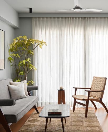 Living room with cane chair, grey sofa, sheer curtains and terracotta floor in Mumbai apartment