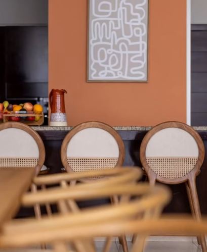 Round cane-back wooden chairs at a dark counter beneath a terracotta wall with abstract art