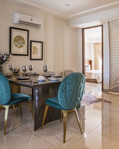 Dining room with marble table, teal velvet leaf-back chairs, and view into bedroom beyond