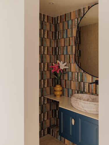 Powder room nook with striped multicolor tile wall, round stone sink, and navy vanity