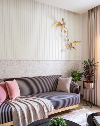 Striped sofa with pink cushions beneath a brass bird-shaped wall sconce on striped wallpaper