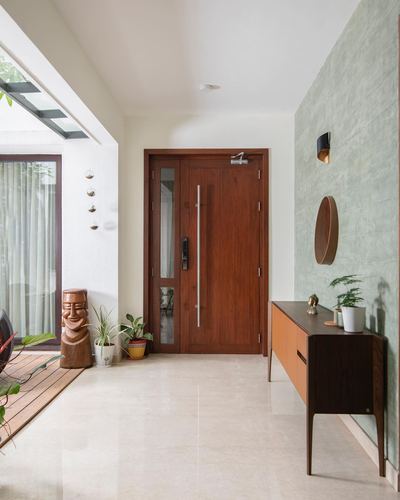 Entry foyer with wooden door, marble floor, green textured wall and mid-century sideboard with round mirror