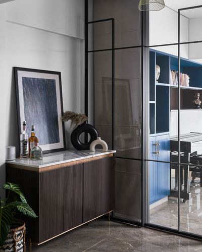 Fluted wood sideboard with marble top beside a smoked-glass partition, blue study visible beyond