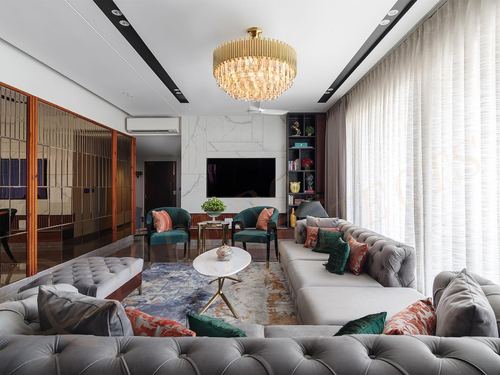 Luxurious living room with tufted grey sofas, emerald chairs, marble TV wall and crystal chandelier