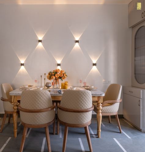 Dining room with marble-top table, quilted cream chairs, and triangular wall sconces casting diamond light patterns
