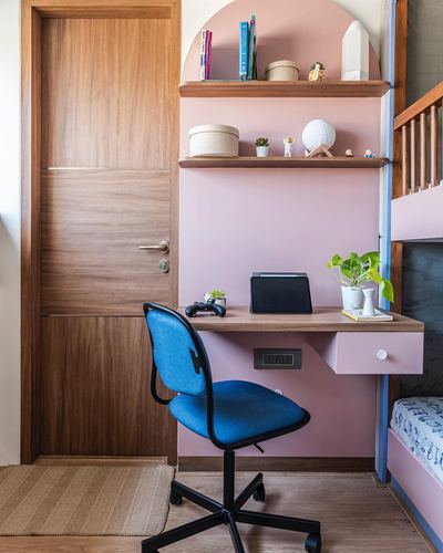Pink arched study nook with floating wood desk, blue chair, and wooden door