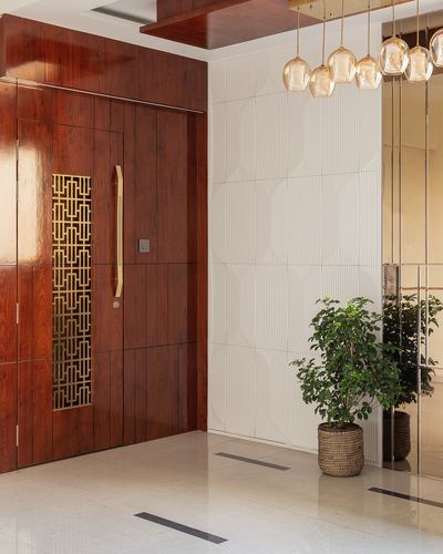 Entrance foyer with reddish wood pivot door, brass jali panel, and hanging amber pendant lights