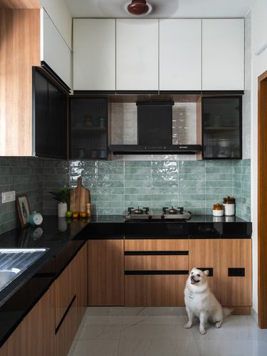 L-shaped kitchen with wood cabinetry, green tile backsplash, black countertop and a dog on the floor
