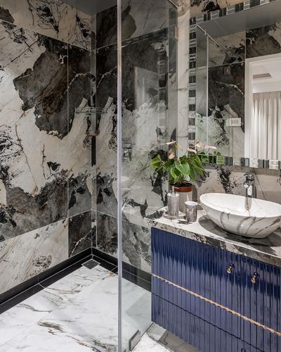 Bathroom with dramatic dark-veined stone walls, glass shower, marble vessel sink and blue fluted vanity