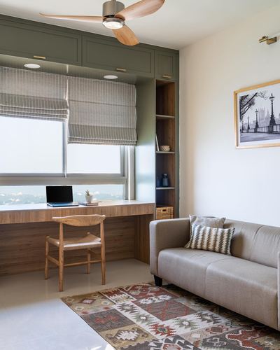 Built-in wooden desk by window with sofa and kilim rug in sunlit study nook