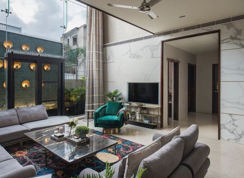 Living room with grey L-shaped sofa, green velvet armchair, and bookmatched marble wall behind TV