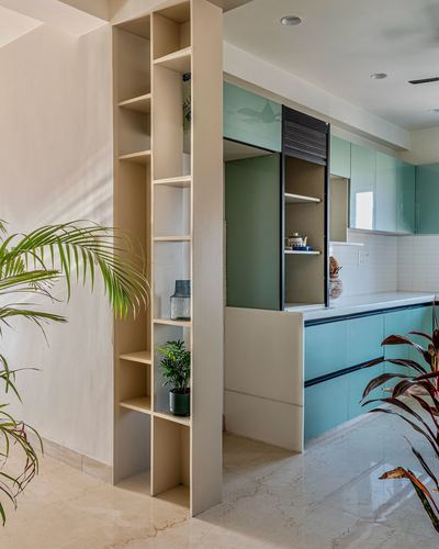 Open shelving divider beside a mint-green kitchen with white countertop in Jaipur home