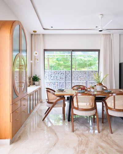 Dining area with teak arched cabinet, cane chairs, and view to gabion garden wall