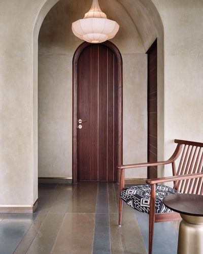 Arched plastered passage leading to a rounded wooden door under a woven pendant light