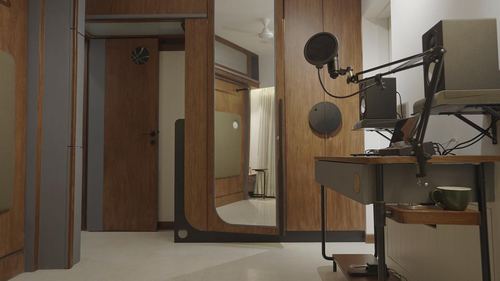 Wood-panelled home studio corner with microphone, speaker, and desk beside a curved doorway