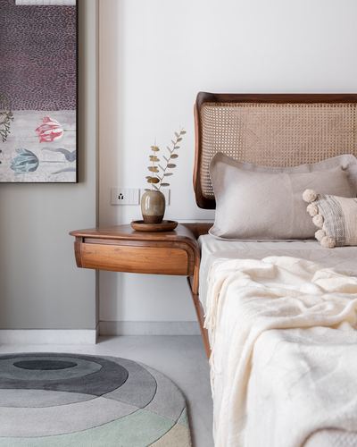 Bedroom corner with cane headboard, floating wood nightstand, vase and layered neutral bedding