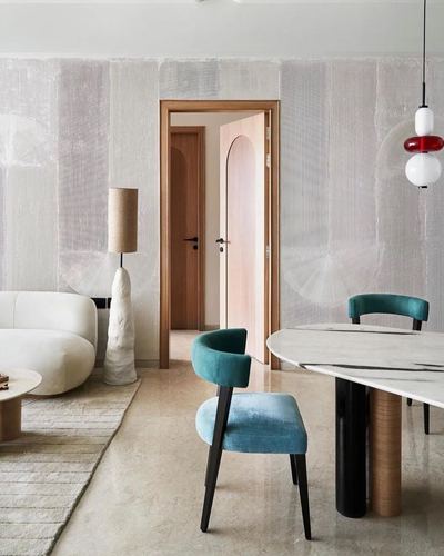Living and dining space with teal velvet chairs, marble table, arched wood door, textured walls