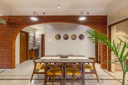 Dining room framed by curved exposed brick archway with wooden chairs and yellow cushions
